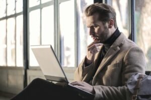 Man looking contemplative while working on a laptop in a well-lit indoor space.