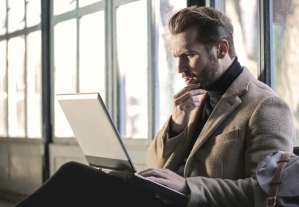 Man looking contemplative while working on a laptop in a well-lit indoor space.